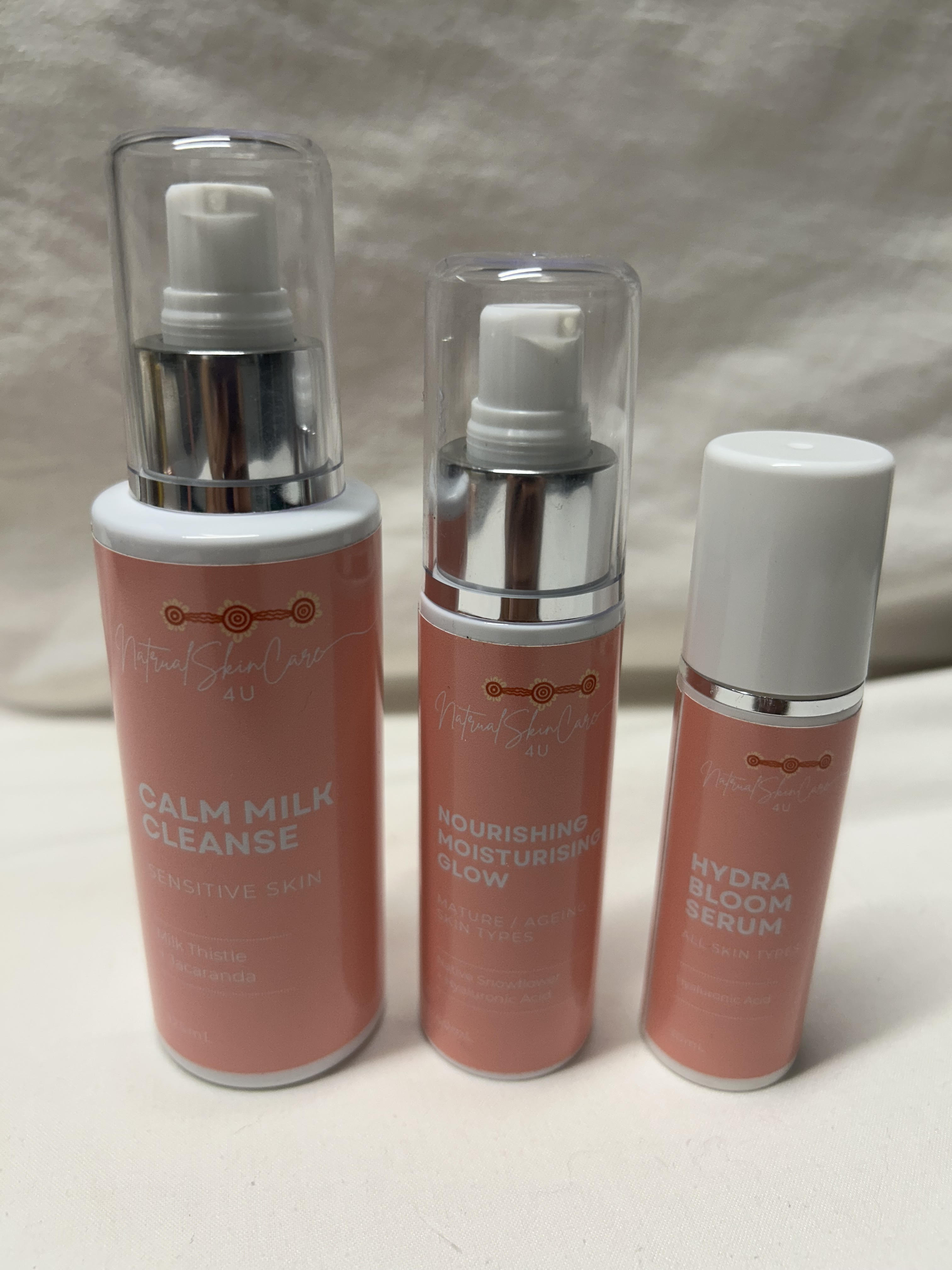 Three skincare bottles labeled 'Calm Milk Cleanse', 'Nourishing Moisturizer', and 'Hydra Bloom Serum' on a neutral background.